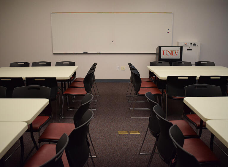 A room with four sets of tables and chairs and a whiteboard