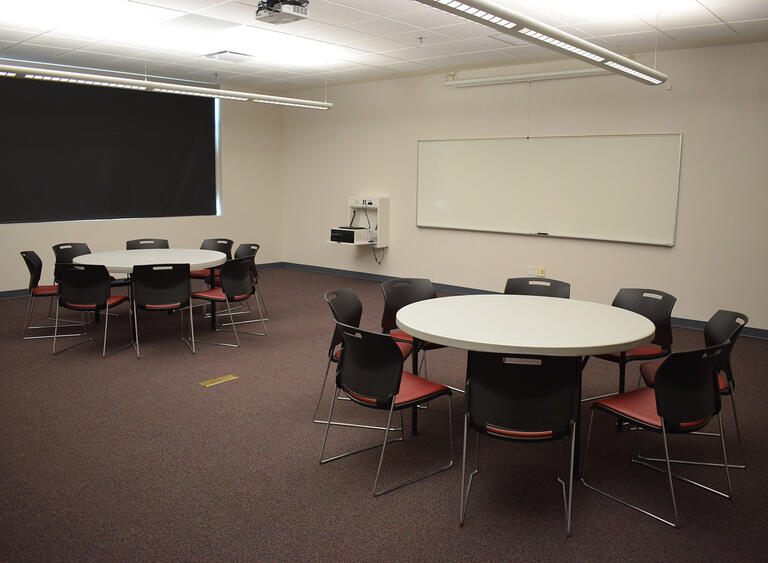 A room with two sets of tables and chairs and a whiteboard