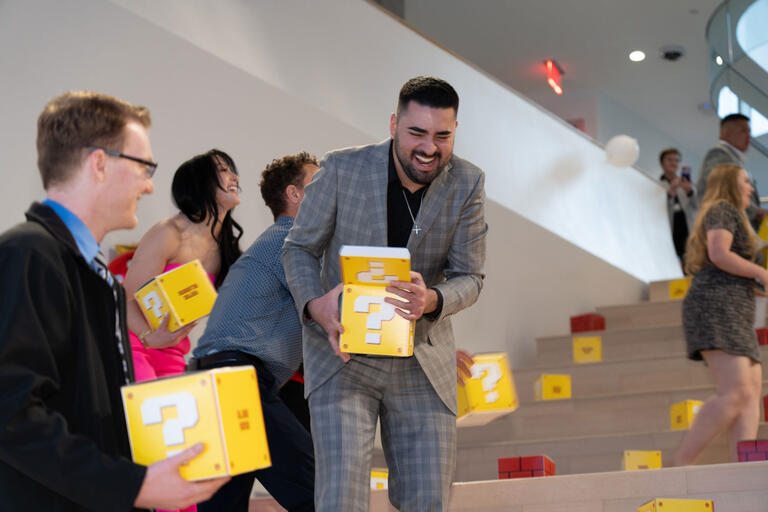 A group of people in formal attire holding yellow "?" block boxes.