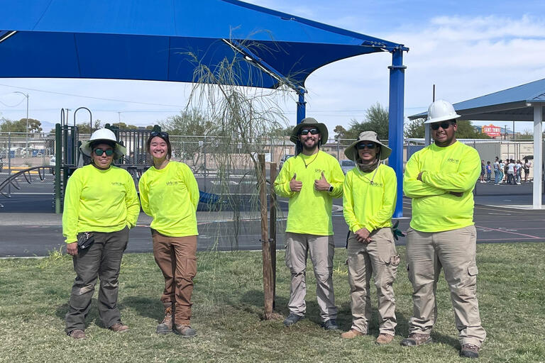 A group posing in front of a newly planted tree.