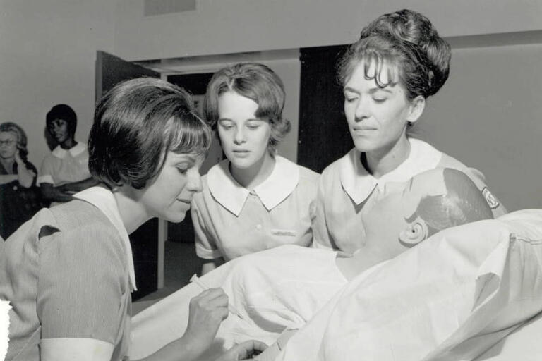 A photo from (likely) the 1960s of three female nurses working on a manikin.