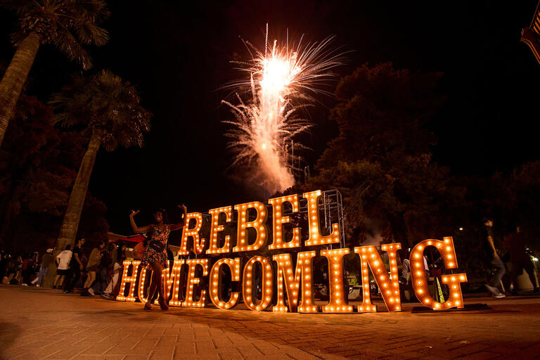 lighted sign saying &quot;Rebel Homecoming&quot; with small fireworks lit up behind it