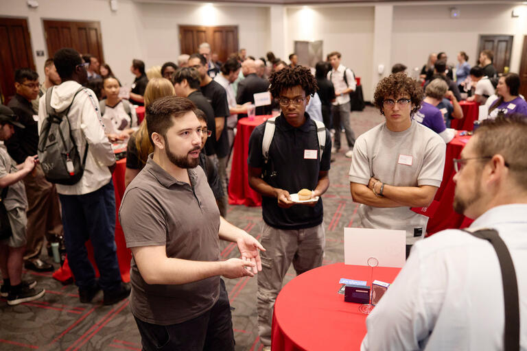 a group of students talk to cyber tech professionals at an event