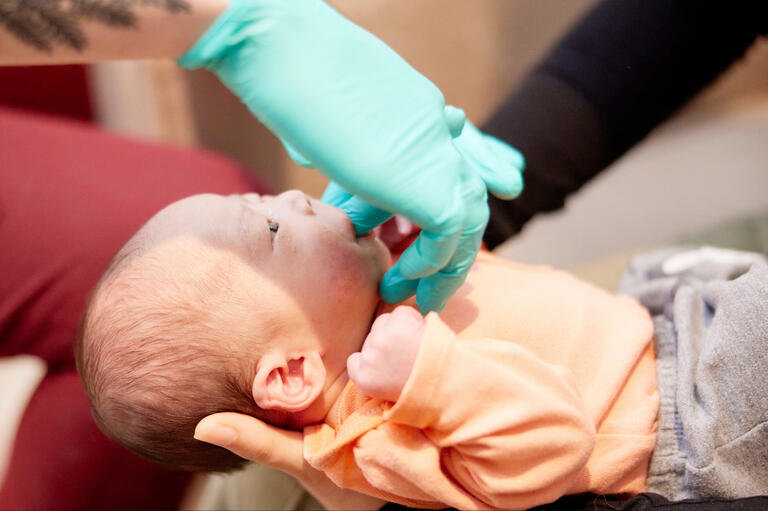 A healthcare provider examines a newborn infant's mouth.