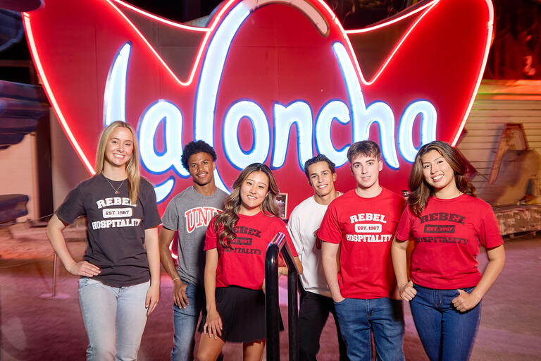 A group of six students stand smiling in front of a large ‘La Concha’ neon sign at night.