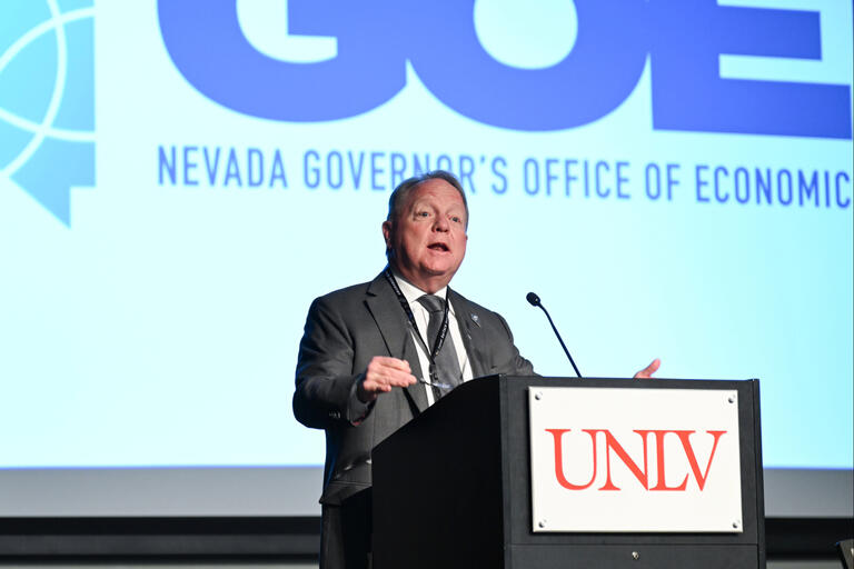 A speaker in front of a projection that reads the Nevada Governor's Office of Economic Development. The speaker's podium has the UNLV logo.