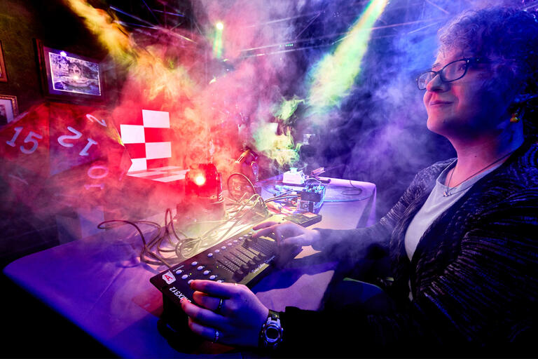 A student adjusts a soundboard while lights and fog machines run in the background.