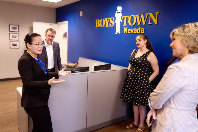 Ying Guo discussing with colleagues in front of wall with Boys Town logo
