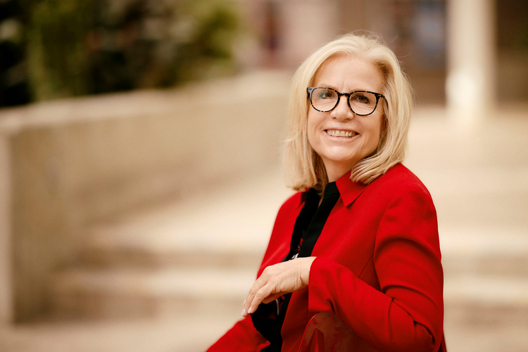 Susan Adair wearing red sweater and glasses while sitting on steps