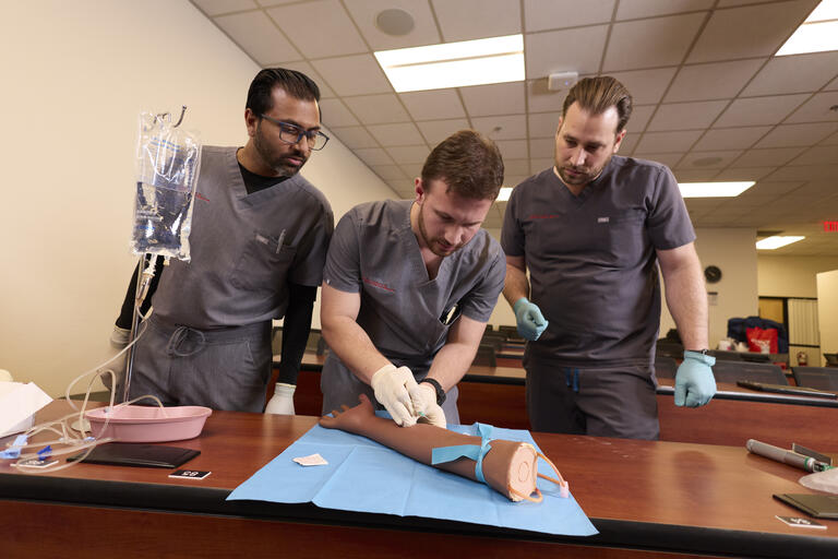 man shows to other male classmates in dental scrubs how to insert an IV
