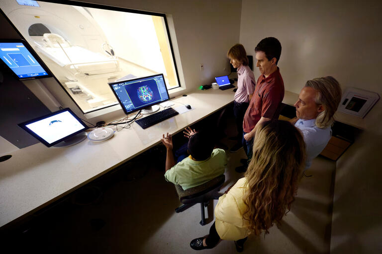 UNLV researchers looking at brain scan peer through glass at fRMI machine