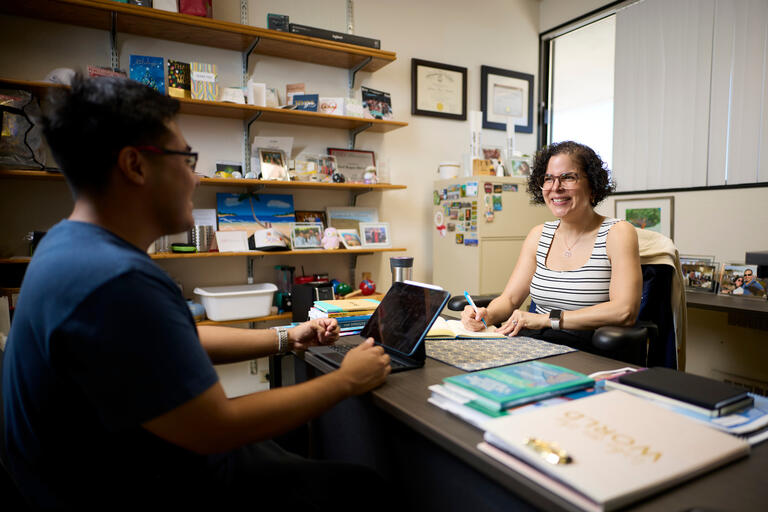 Gloribert Roque-Melendez sits at a desk in her office talking to student