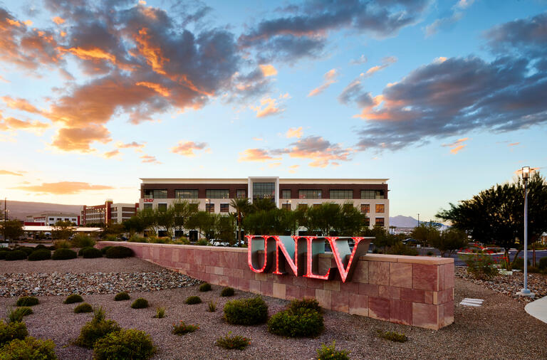 UNLV sign in foreground of four story building with clouds above