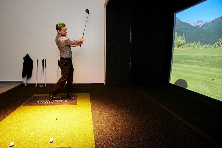 A student playing golf on a simulator screen.