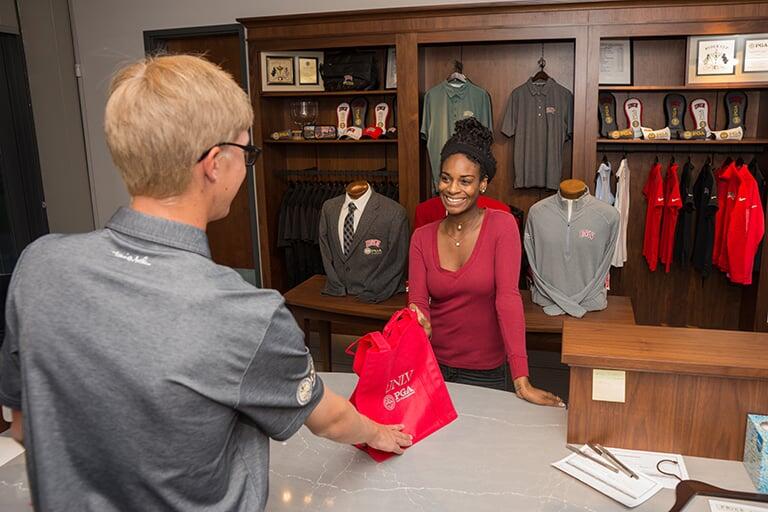 A retail store with golf merchandise being purchased by a customer.