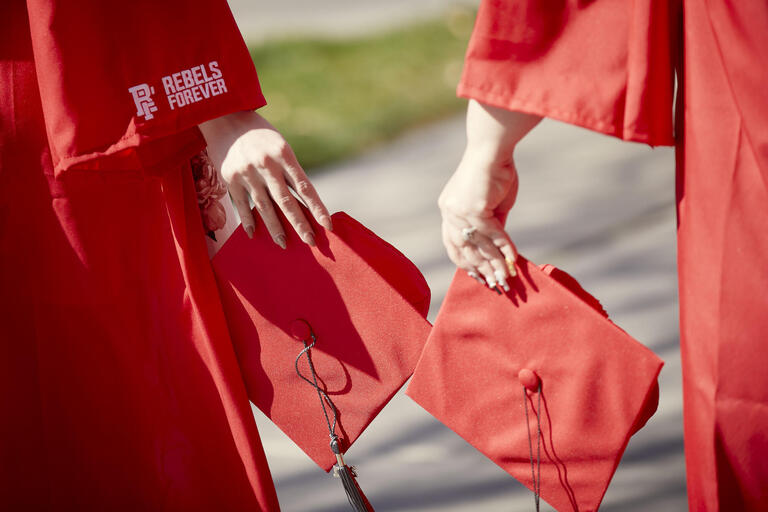 A close-up image of two UNLV grads holding their red UNLV mortarboards for commencement photos on campus