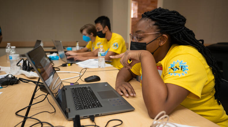 A local Las Vegas high schooler in a yellow shirt participates in an cybersecurity activity on a laptop