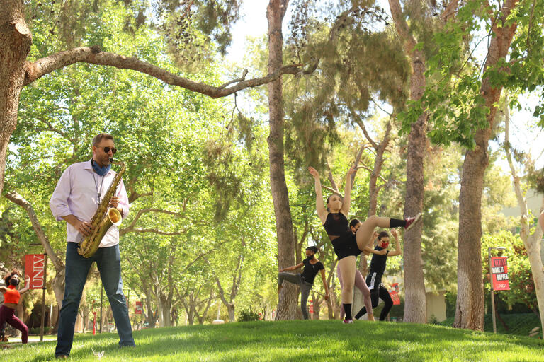 A man plays the saxophone while dancers gambol around him