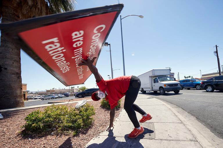 A man holds a sign over his head with one hand while the other is on the ground
