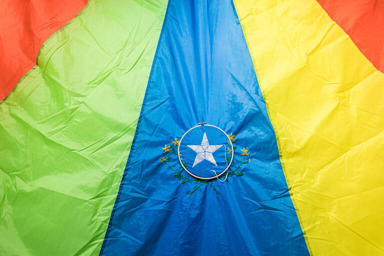 A colorful work of embroidery features a white star on a blue field