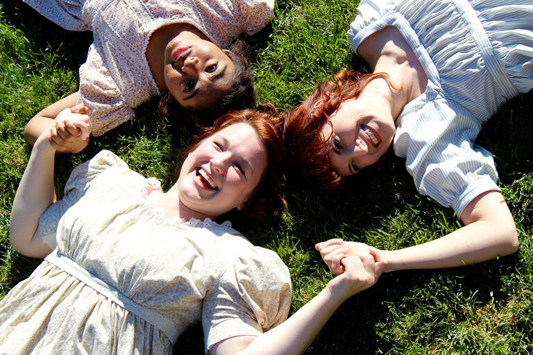 Christina Harvey, Therese Anderberg, and Alexandra Ralph lay in the grass, holding hands