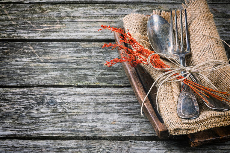 fork and knife tied together with string lay atop a napkin that rests on a wooden plate