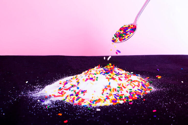 spoon pours candy sprinkles atop pile of white sugar