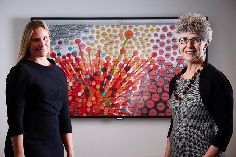 Cory Lampert and Silvia Southwick pose in front of a colorful data display