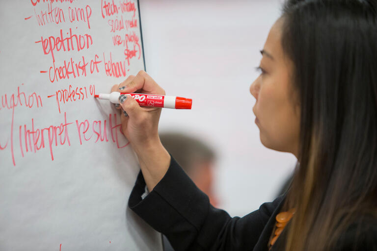 A woman writing notes on a blackboard with an orange marker.