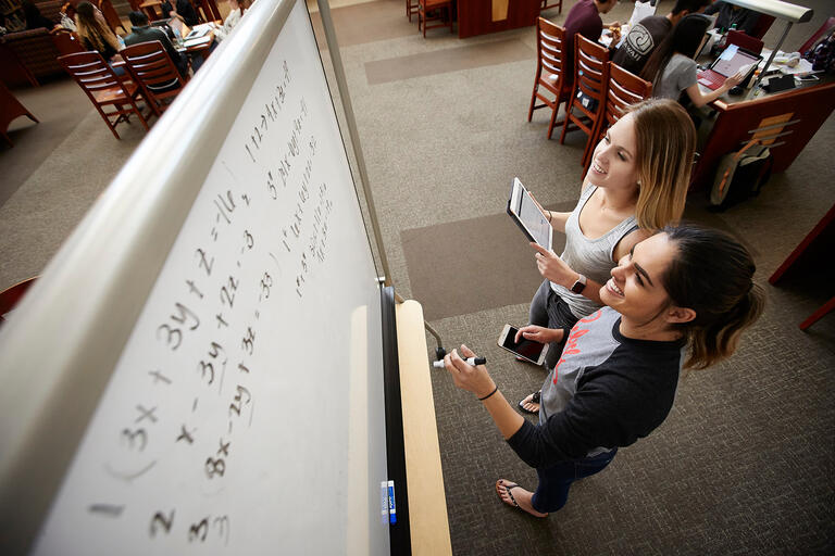 Two women working on a math equation on a blackboard.