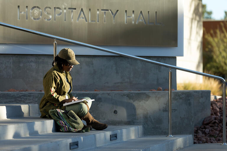 A student studying cultural studies on the stairs leading up to Hospitality Hall.