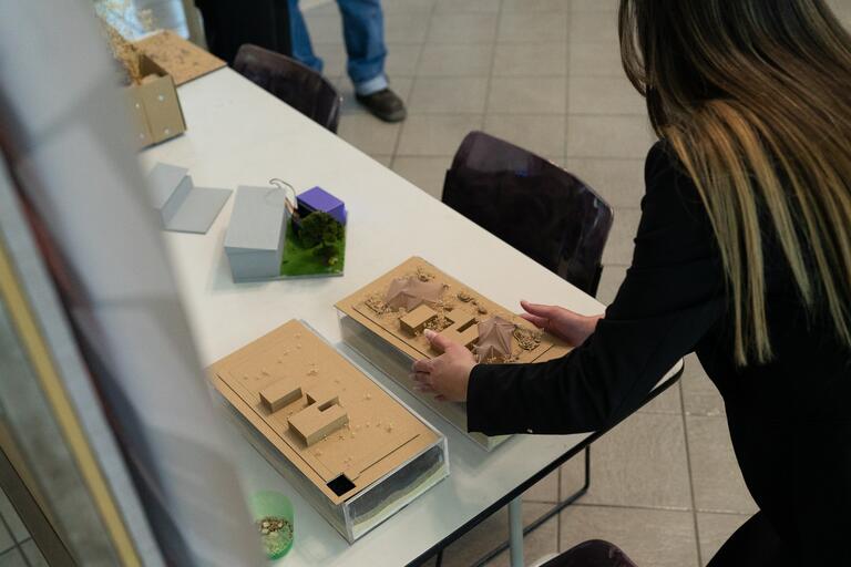Photo of Architecture student placing a model of a building on a classroom table