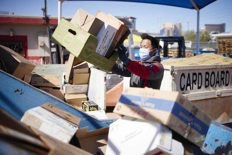 man wearing masks organizes piles of cardboard for recycling
