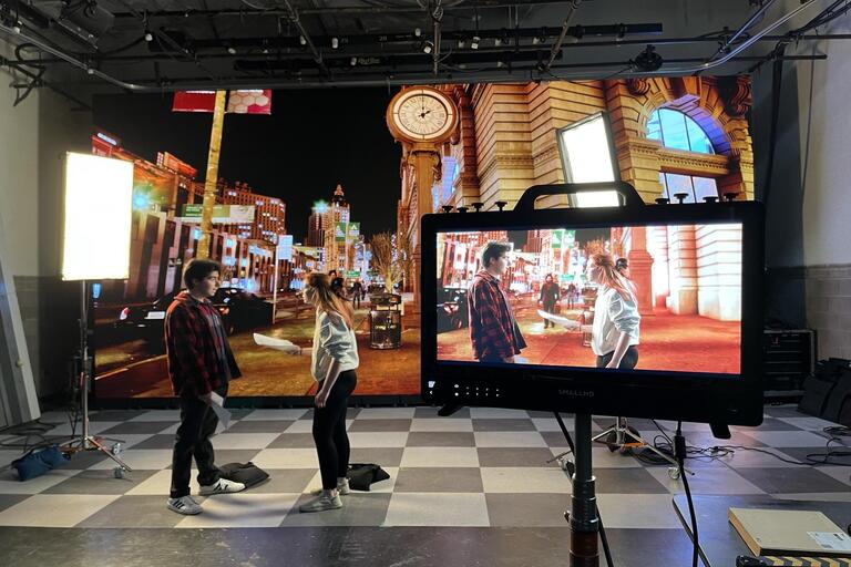 two actors on a soundstage in front of an LED wall projecting a city scene.