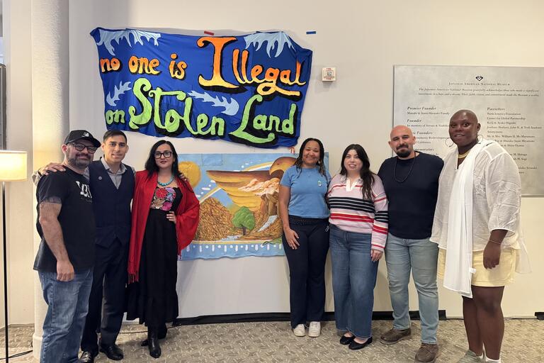 A group of people of all types smiling to the camera as they stand in front of artwork