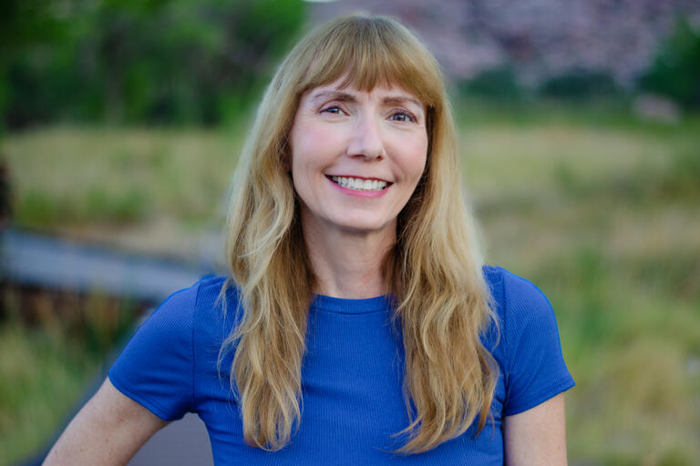 Blonde woman with bangs and a blue shirt smiles to the camera