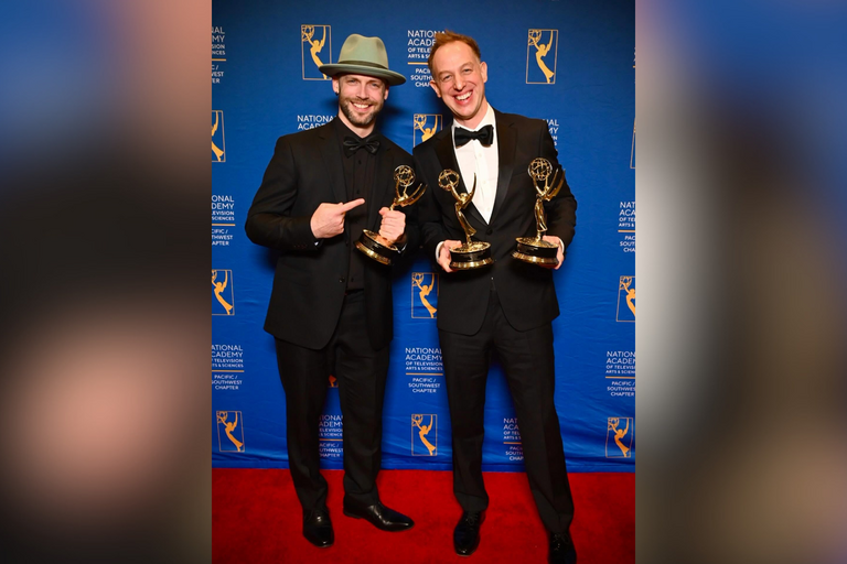 Two men on a red carpet holding up Emmy award trophies
