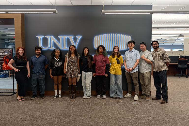 Photo of students and faculty smiling in front of a lit UNLV sign