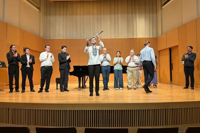 Musicians on stage clapping for someone in the middle of the stage holding up an instrument