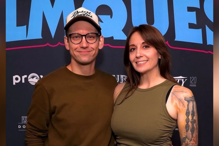 Man and woman smiling at the camera in front of a step and repeat banner