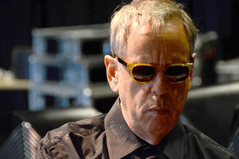 Photo of man with glasses. Piano keys are reflected in his glasses.