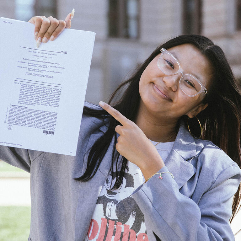 woman posing outside holding up a legal document and pointing to it