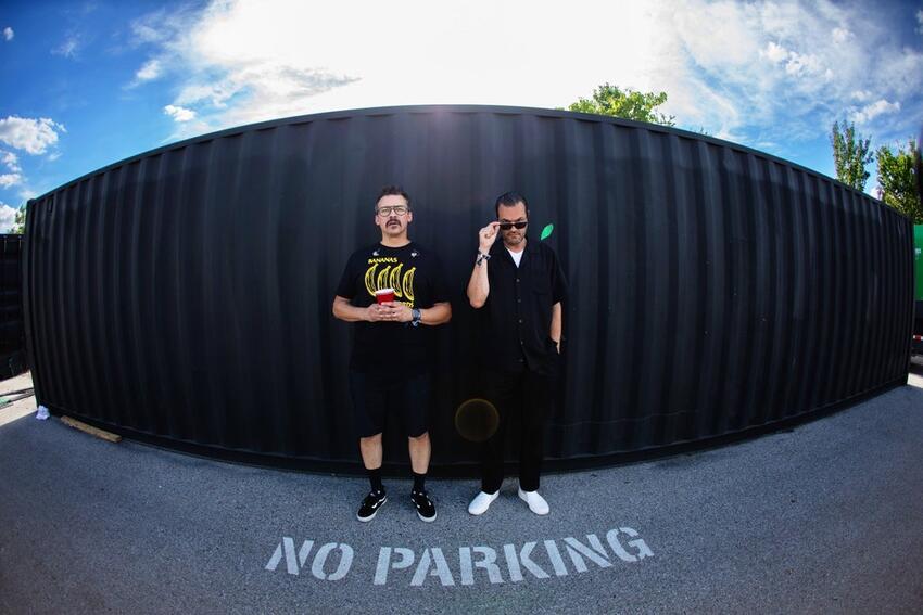 Members of Atmosphere (Slug [Sean Daley] and Ant [Anthony Davis]) pose in front of a large storage container.