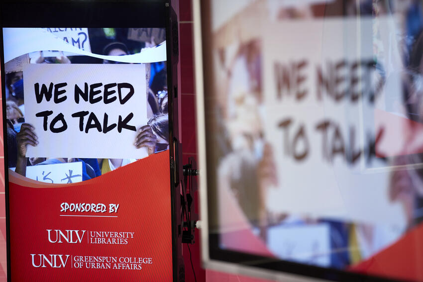 Digital screen displaying an image of a person holding a sign that reads "we need to talk."