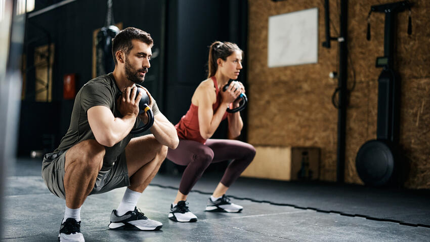 A man and woman squatting with kettlebells