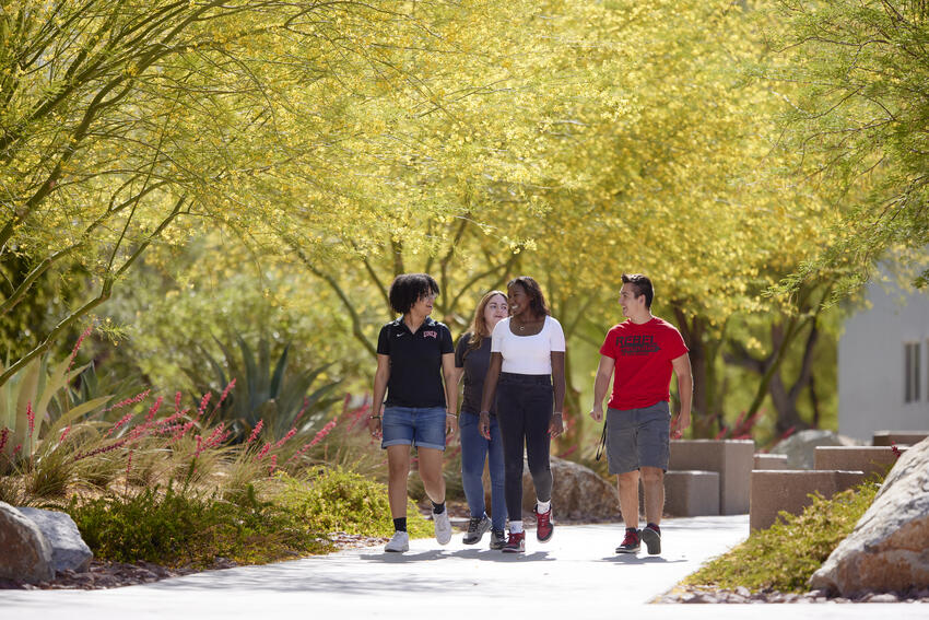 Four UNLV students walk and talk together by the Student Wellness and Recreation Center.