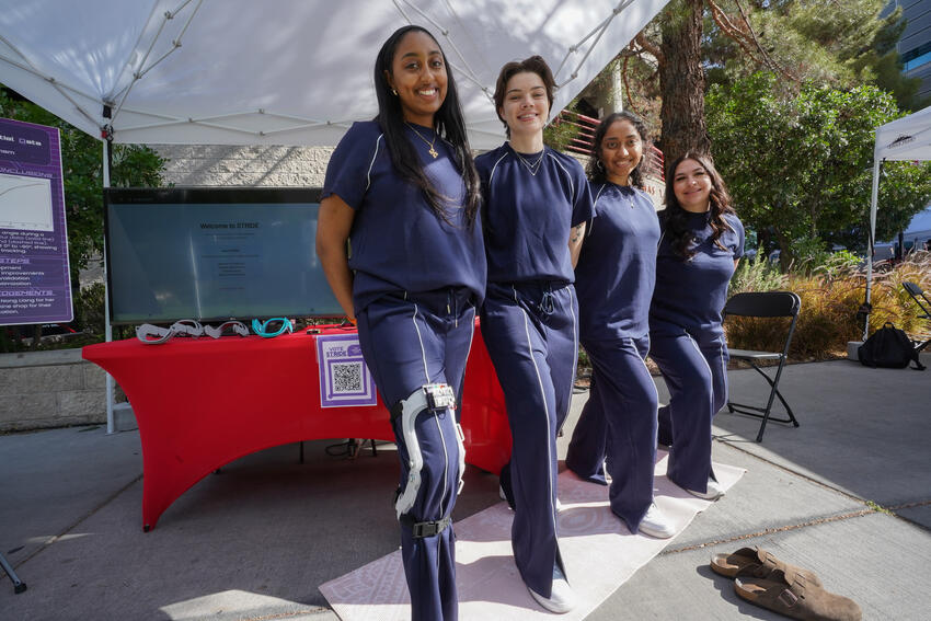 Four students stand in front of their booth at the design competition