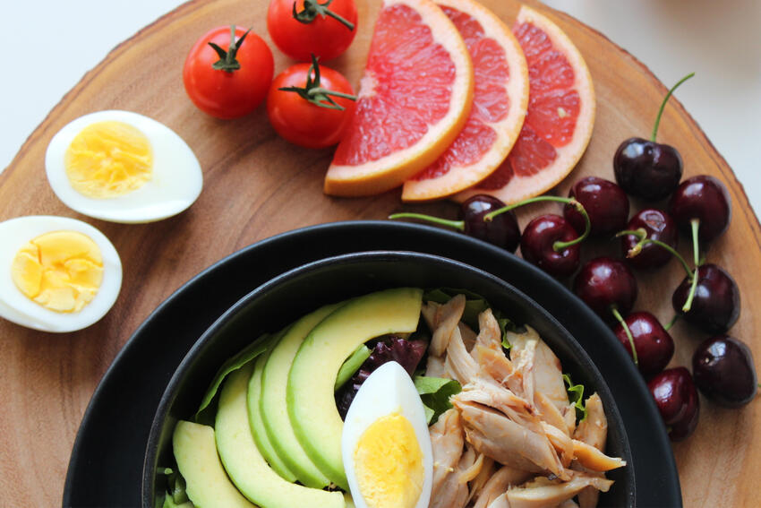 Hard-boiled eggs, grapefruit, cherries, and a bowl with avocados and chicken resting on a table.