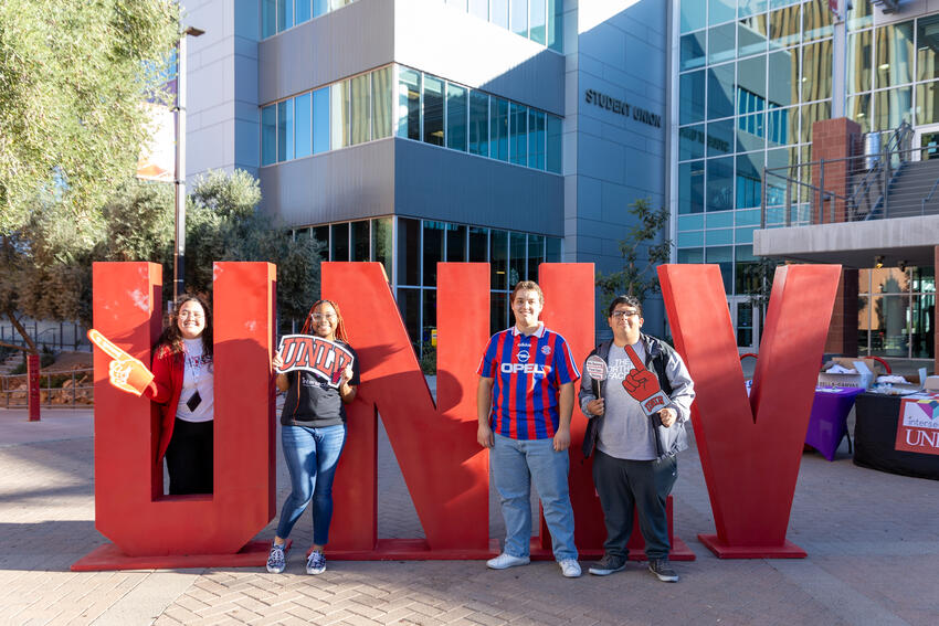 Four students posing in front of the large UNLV letters