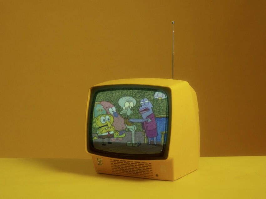 A retro yellow television placed on an all-yellow background. The television displays the &quot;Opposite Day&quot; episode of Spongebob Squarepants where Spongebob and Patrick impersonate Squidward. A purple real estate fish is angrily speaking to Spongebob, Patrick, and Squidward.
